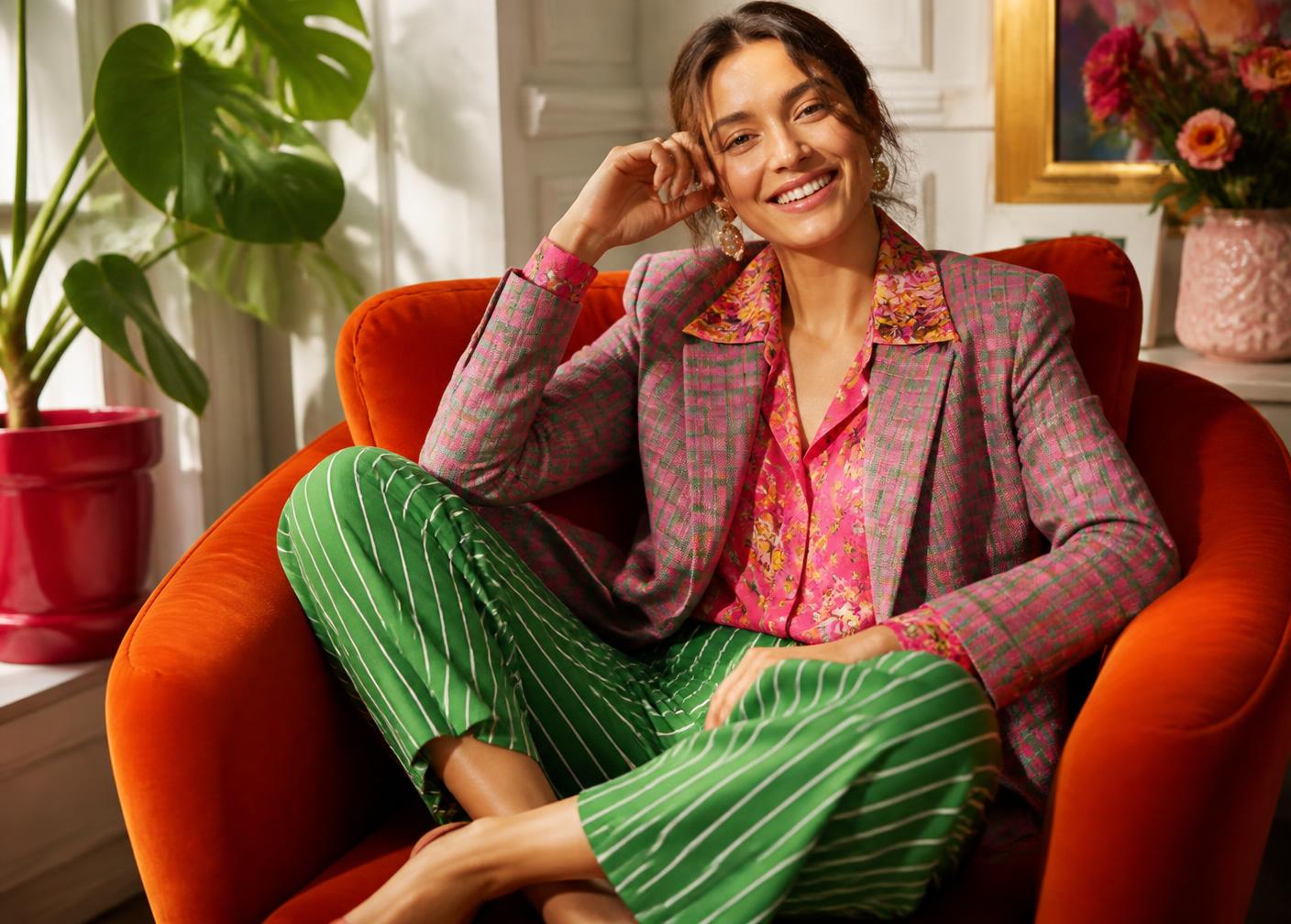 Model in a colour-blocked printed suit seated on a bright modern chair