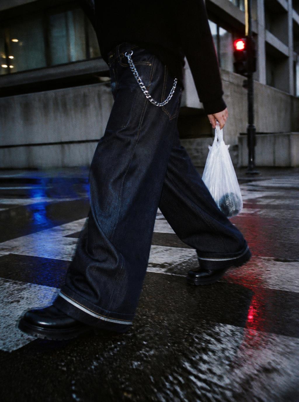 Wide leg indigo denim jeans and chunky boots mid stride on a wet neon lit crosswalk